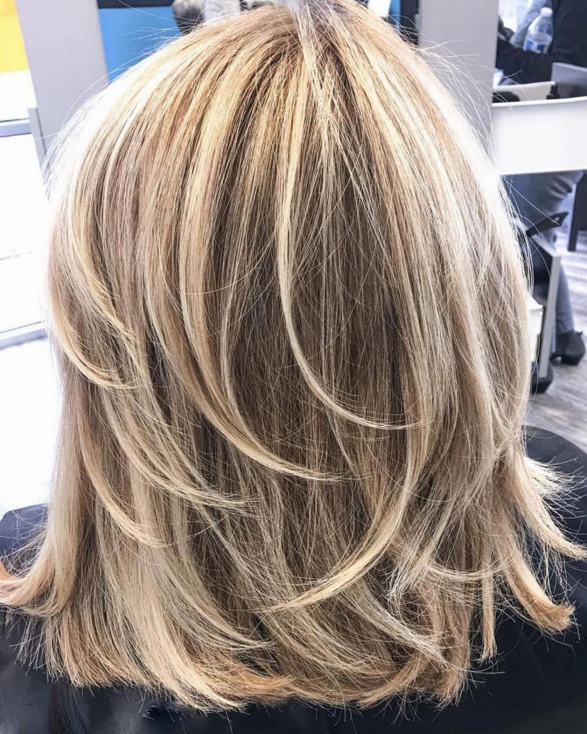 Feathered blonde layers curve around the shoulders with airy, tapered ends