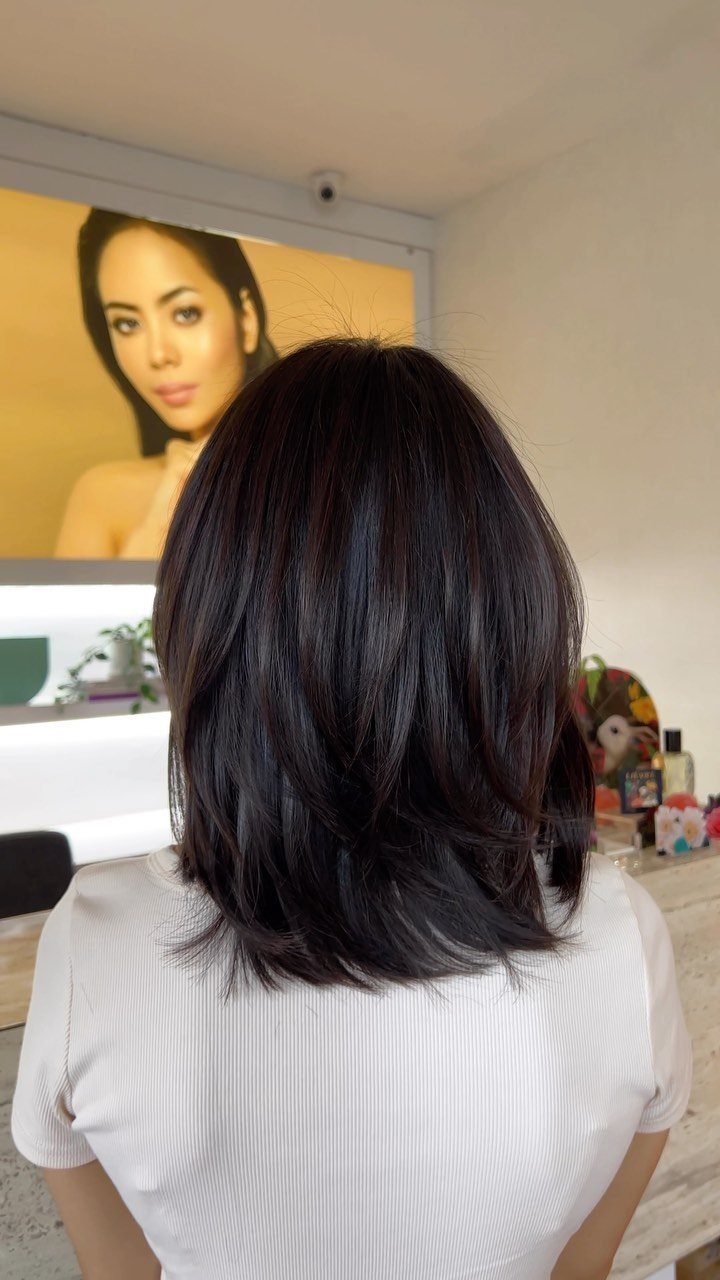 Layered long bob with dark hair viewed from behind in a salon
