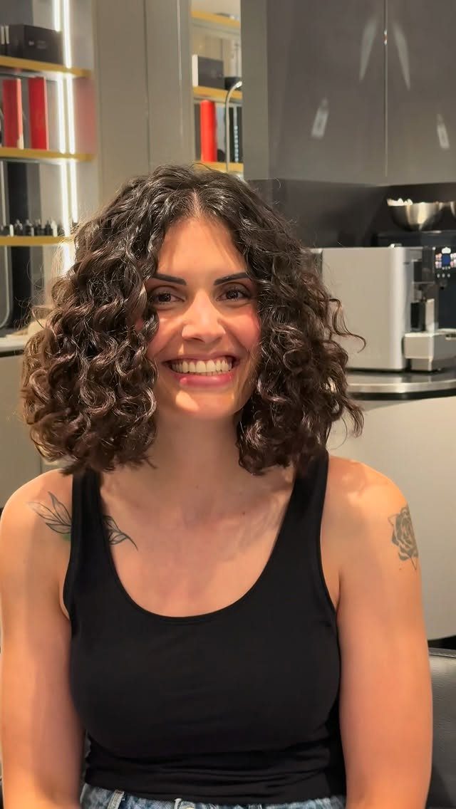 Woman with dark medium-length curls smiling in a salon