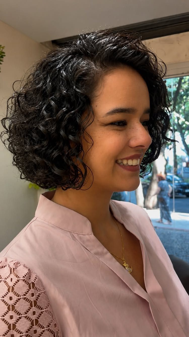 Curly bob haircut frames a smiling person’s face indoors