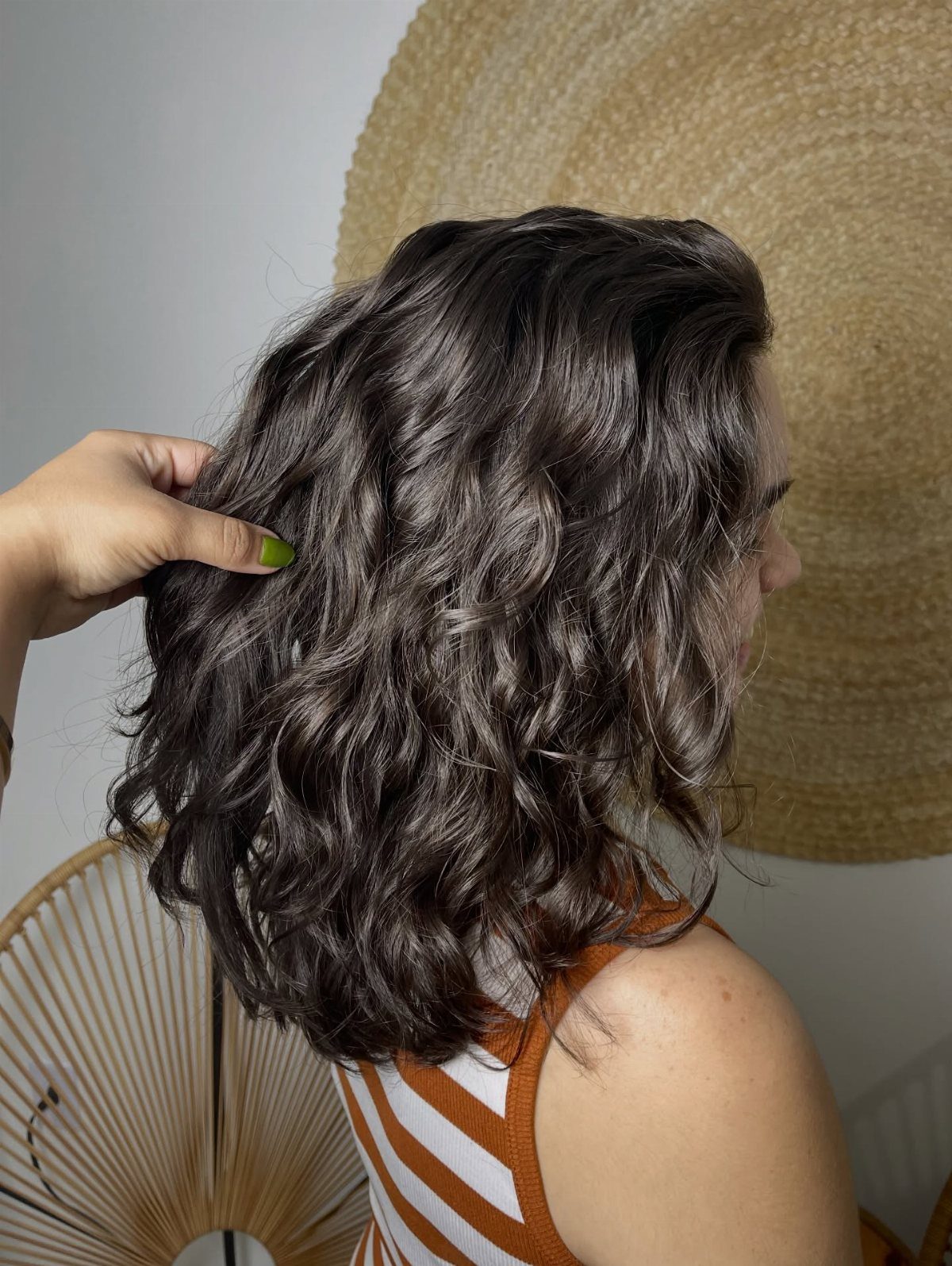 Dark, textured shoulder-length waves shown from behind as a hand lifts the hair