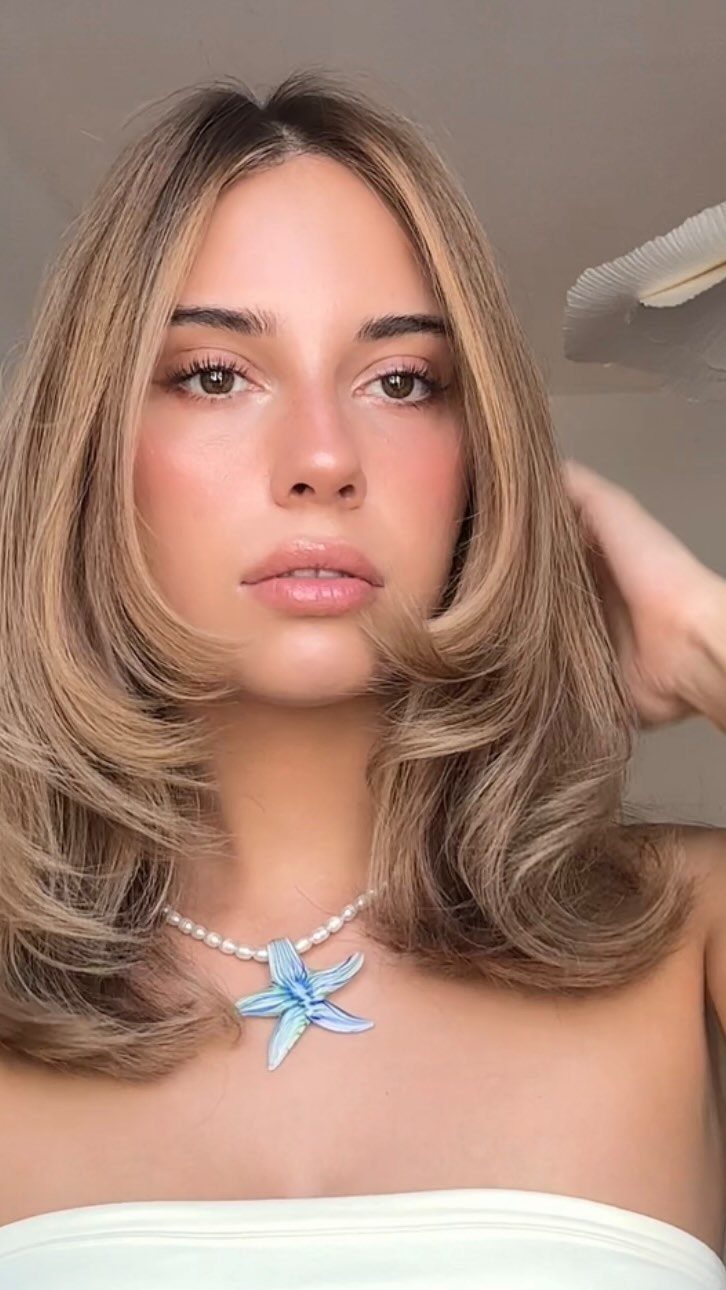 Long blonde hair styled in a sleek, layered Rachel cut with outward-flipped ends