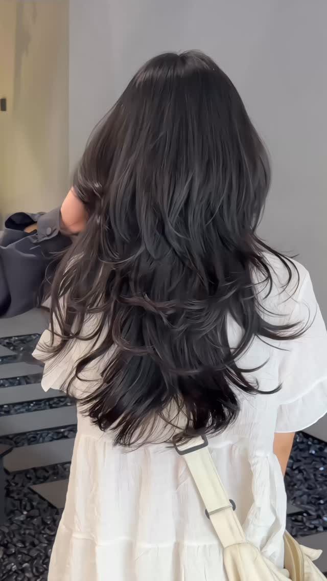 Long dark hair with choppy, textured layers falling over a white top