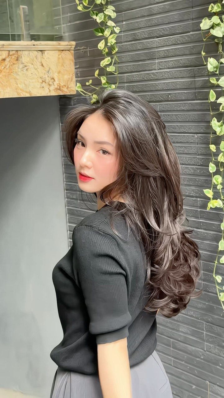 Woman showing long dark hair with face-framing layers and curled ends