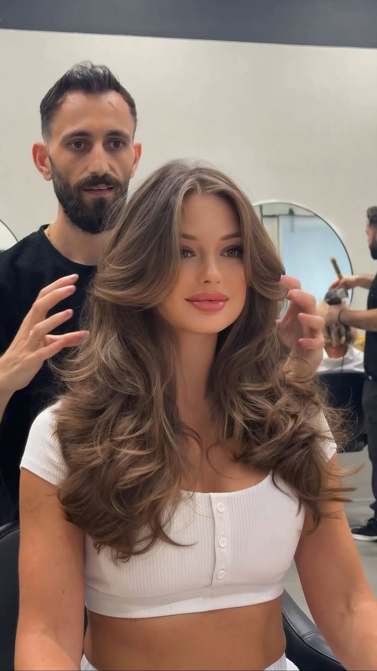 Woman with long brown hair styled in voluminous swooping layers at a salon