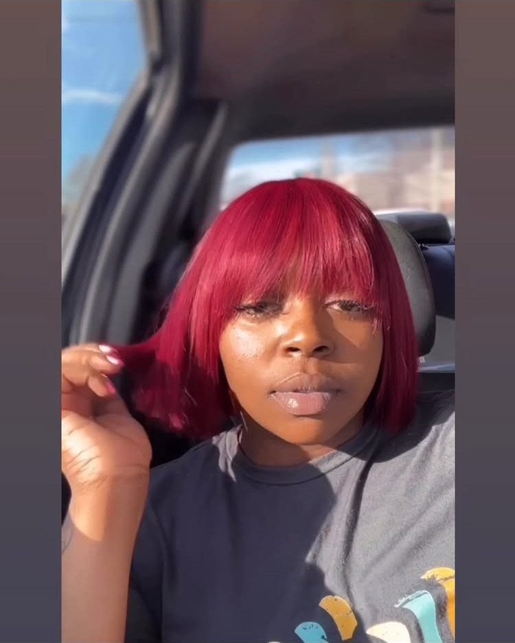 Red blunt bang bob frames a person's face as they sit in a car