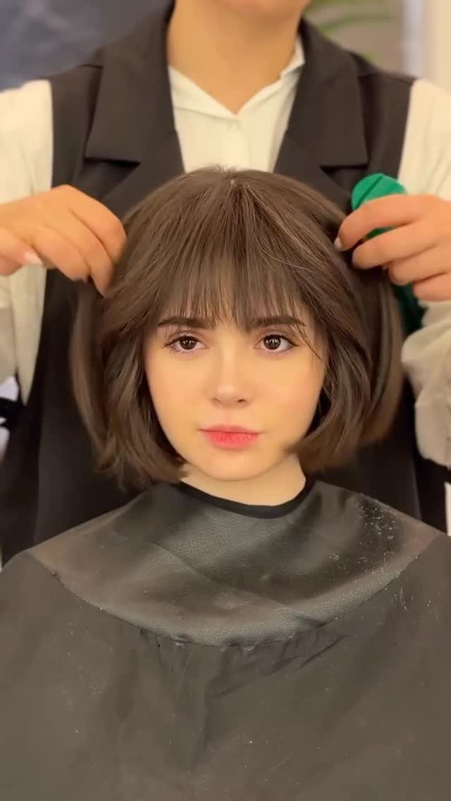 Young woman with a short brown French bob and straight bangs in a salon