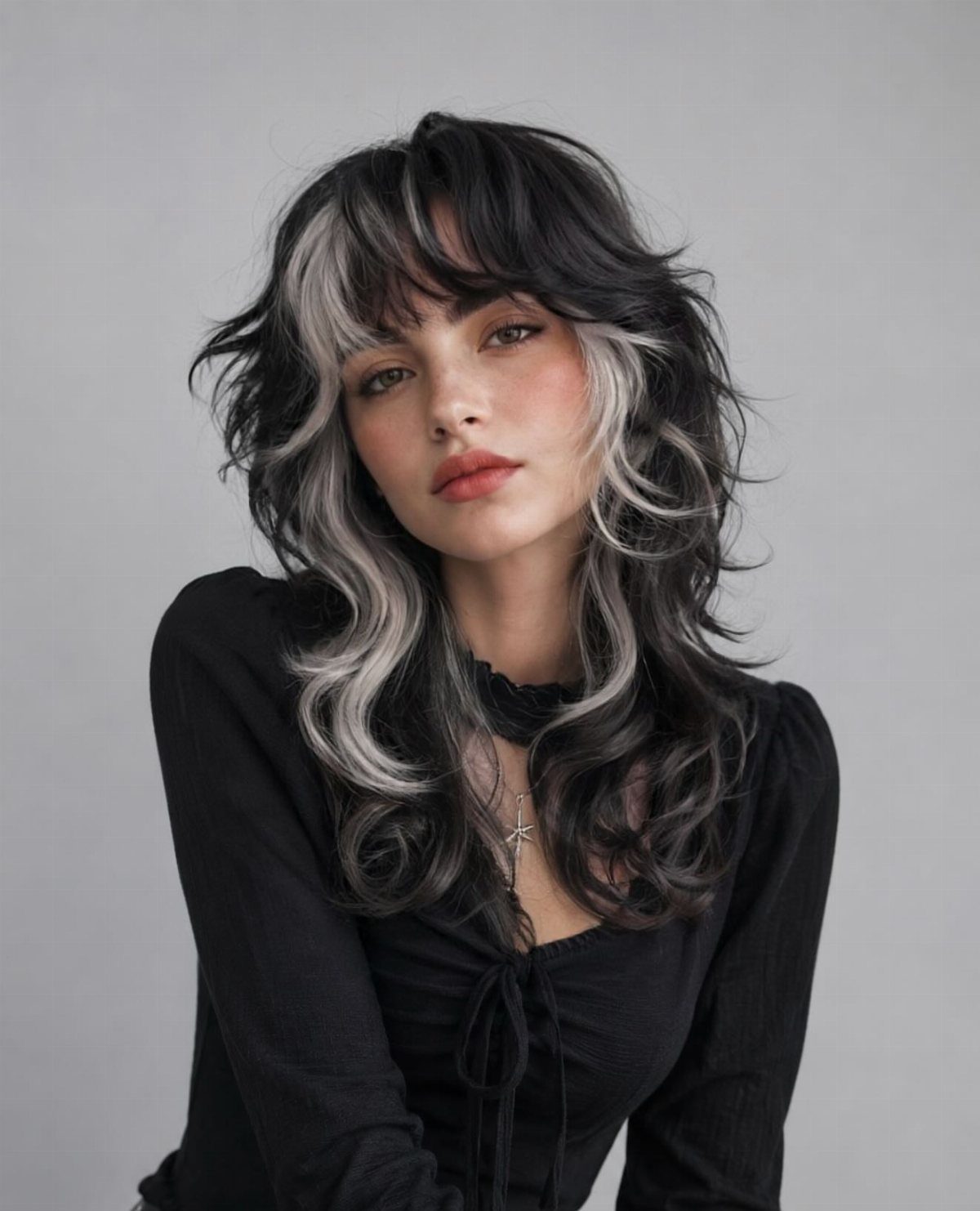 Woman with layered black hair, wispy bangs, and contrasting silver-gray streaks