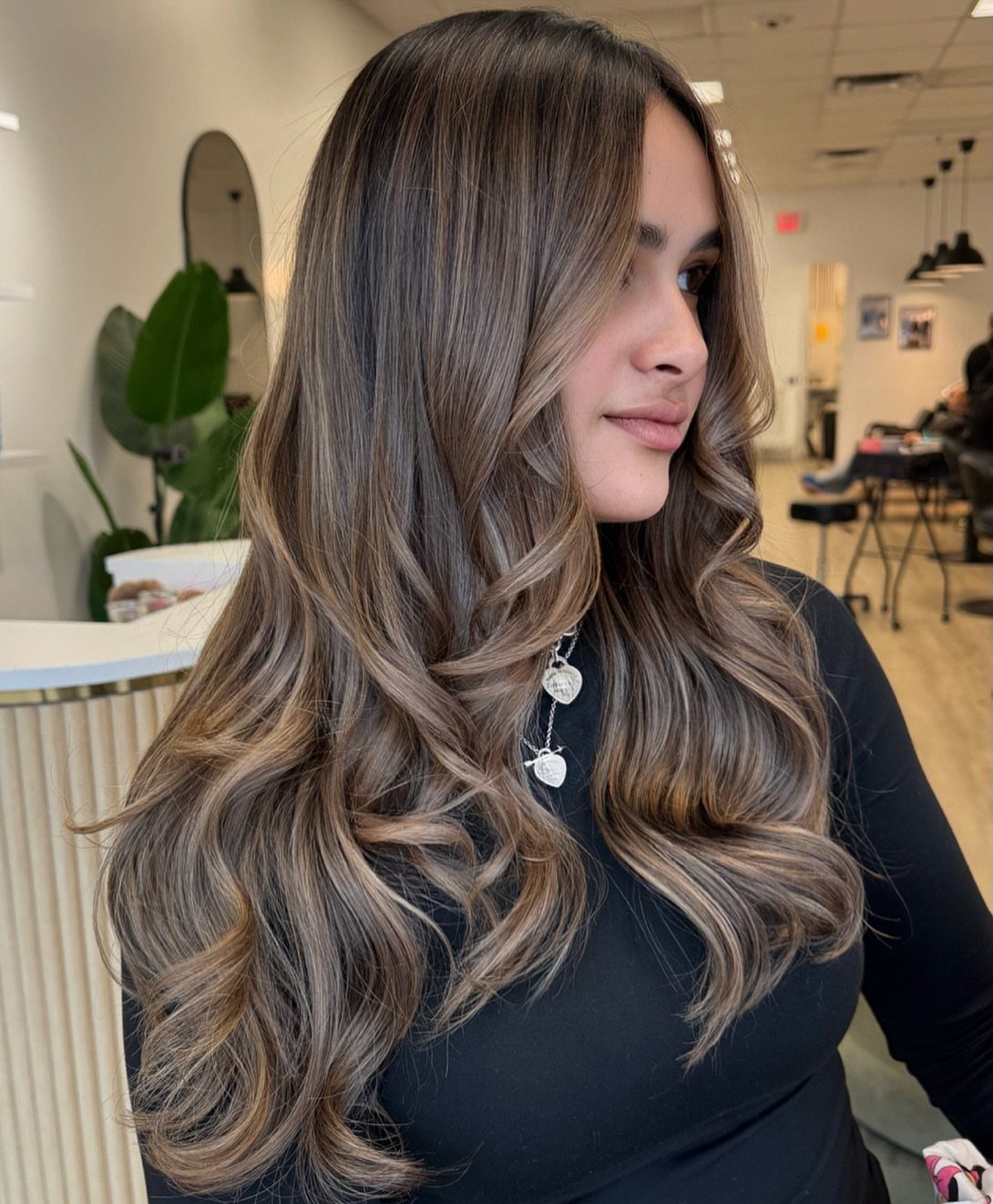 Woman with long brown hair styled in soft curls and beige-blonde highlights