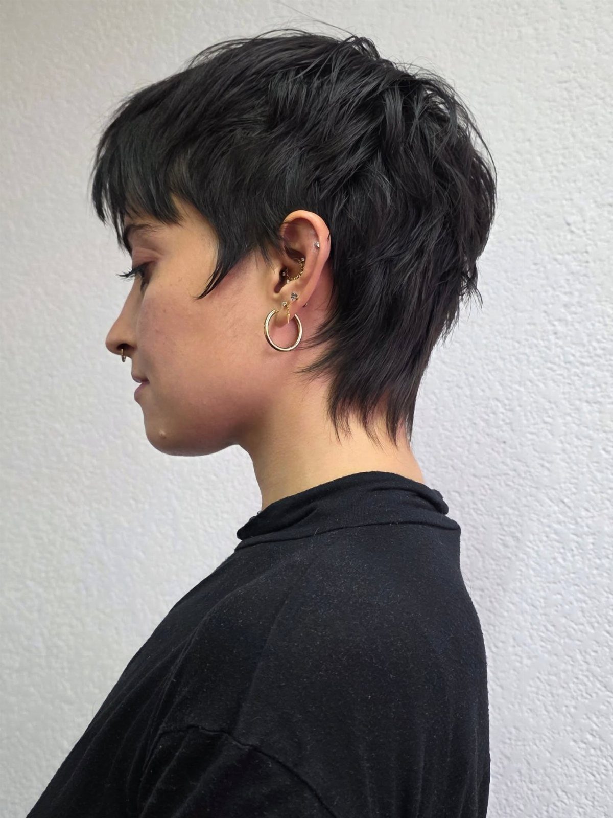 Short dark pixie haircut with tousled bangs shown in side profile