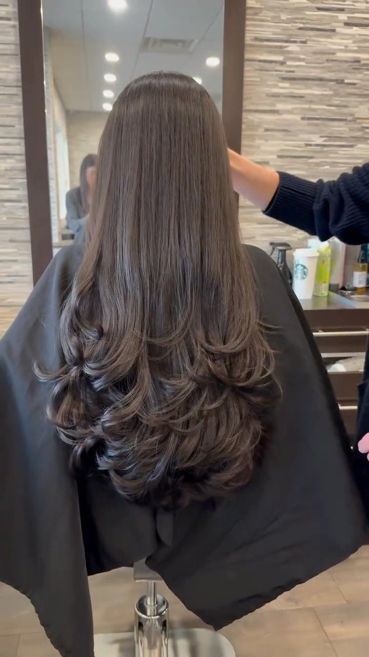 Long brown hair with smooth upper layers and curled, feathered ends in a salon chair