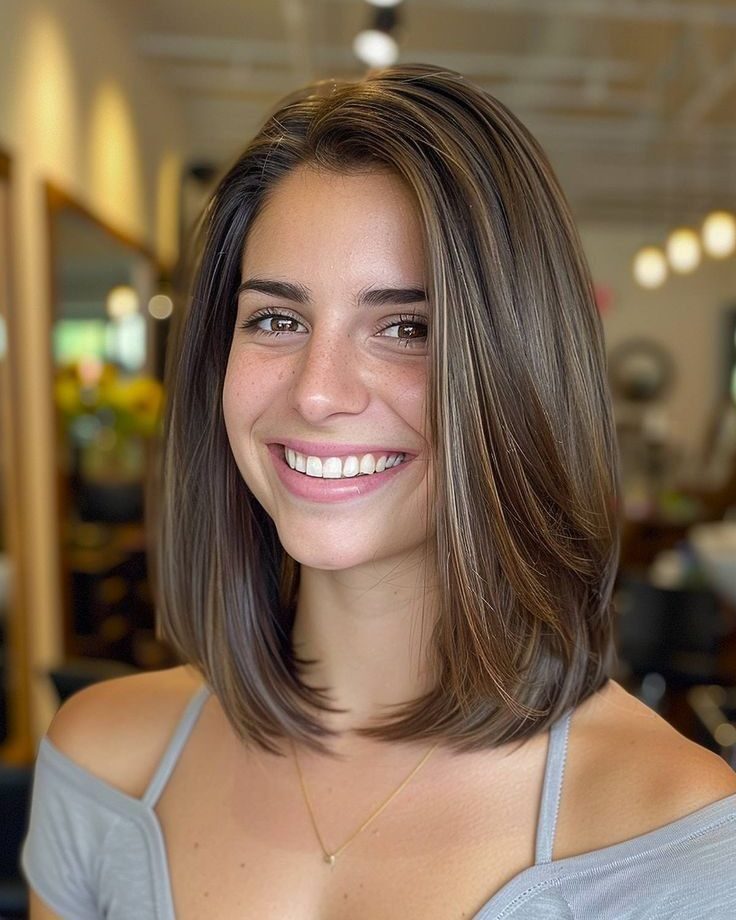 Woman smiling with straight, shoulder-length brown hair parted in the center