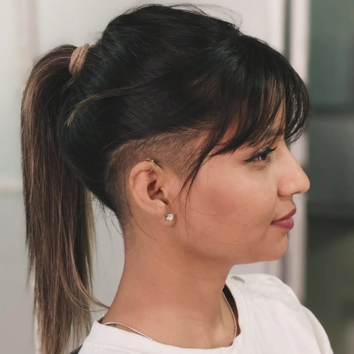 Woman with a high ponytail showing a closely buzzed side and long bangs