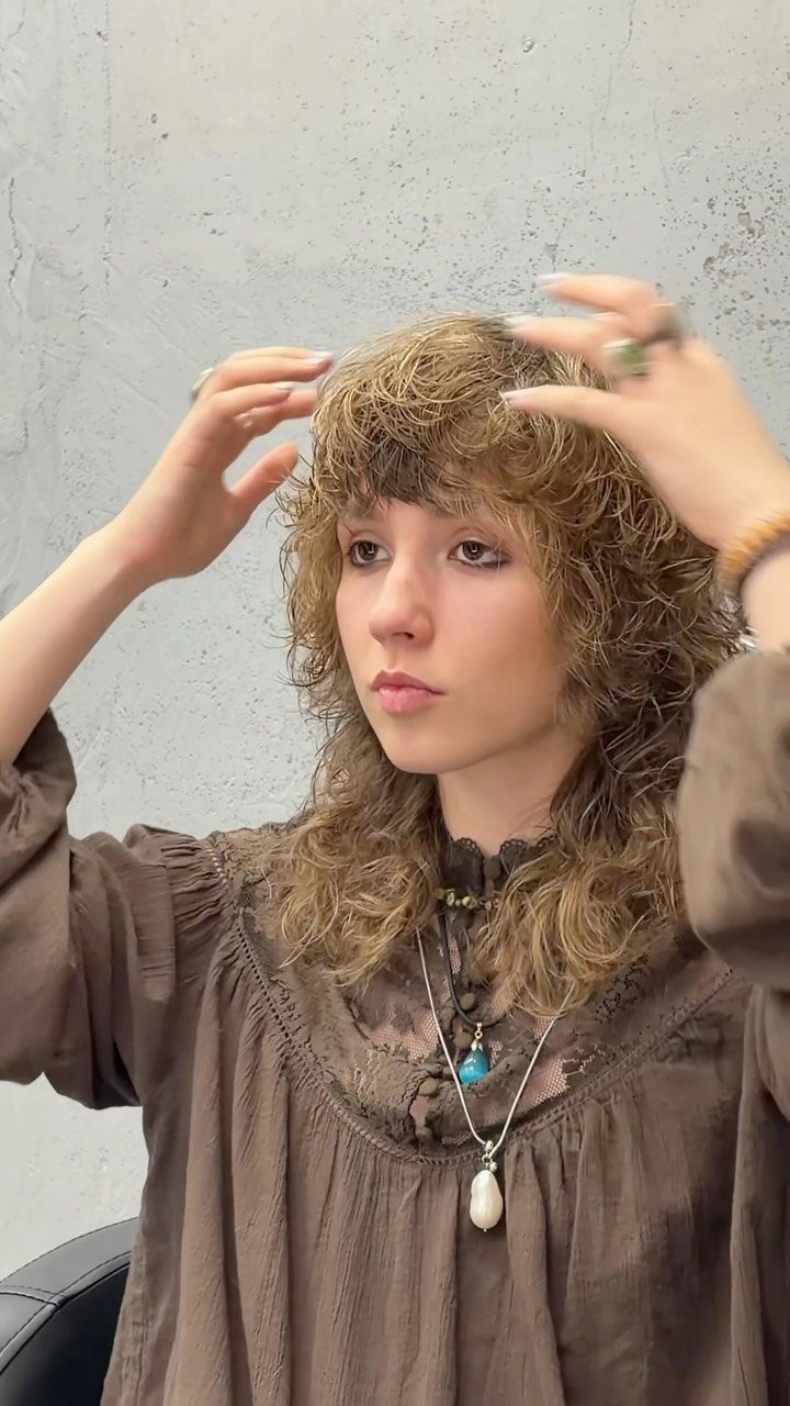 Person with long curly hair and bangs adjusting curls at the crown