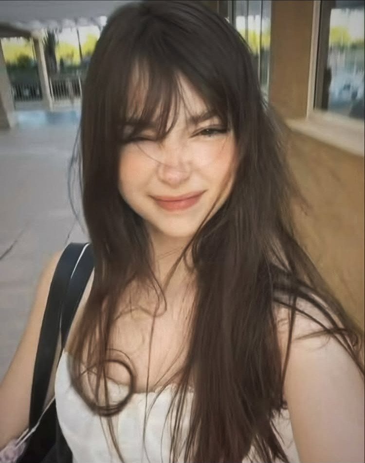 Woman with long dark layered hair and wispy fringe bangs smiling indoors