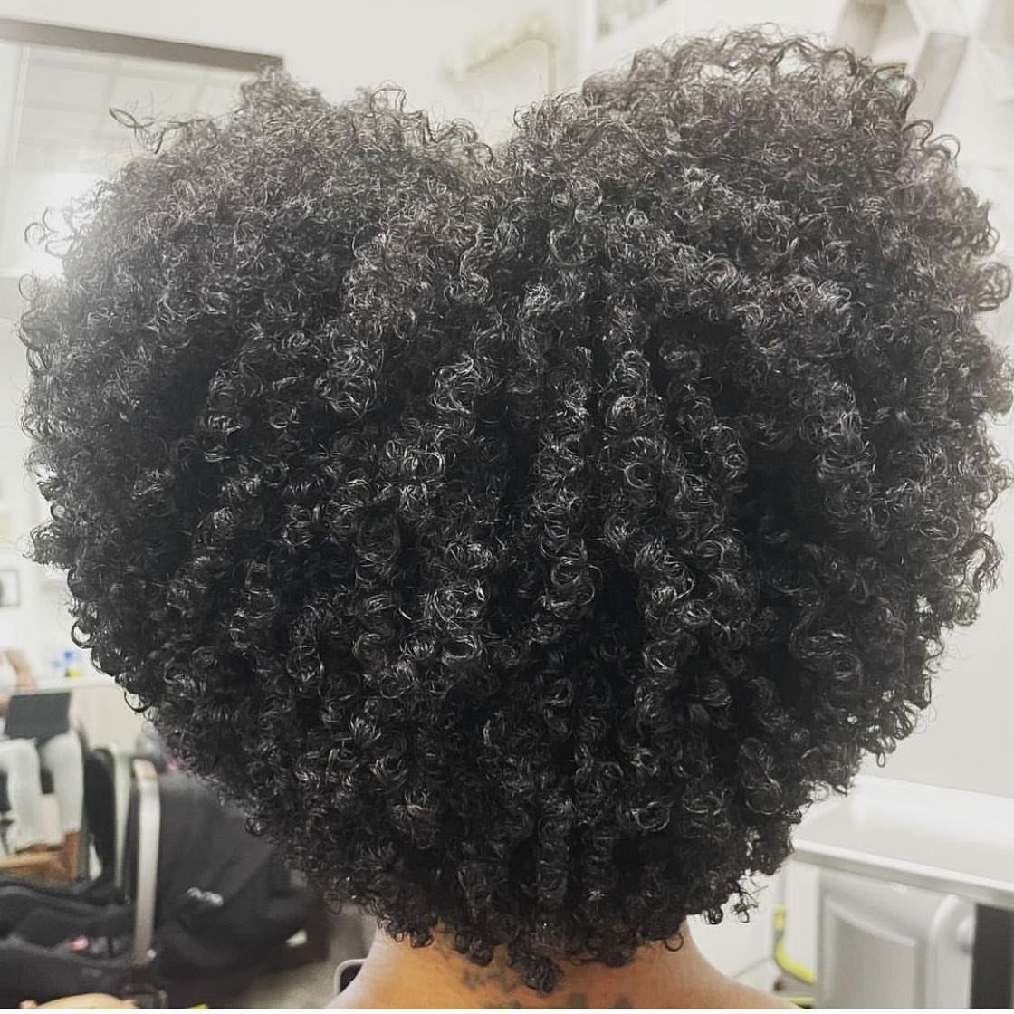 Heart-shaped afro with dense dark curls seen from behind in a salon