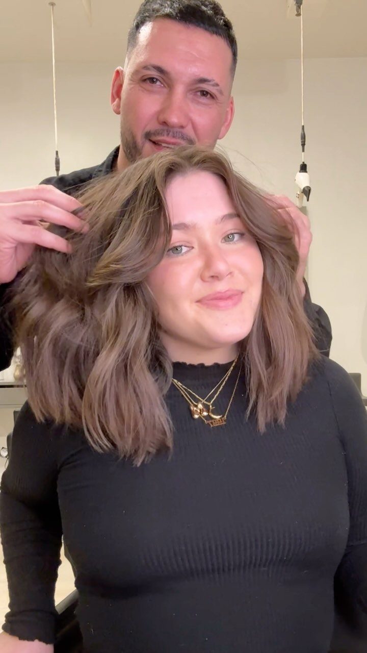 Woman showing a layered shoulder-length wavy lob while a stylist lifts her hair