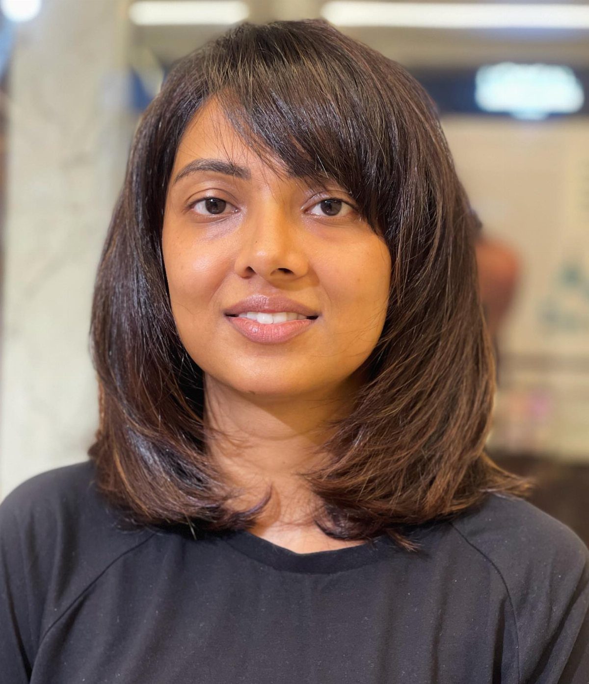 Woman with shoulder-length layered hair and side-swept bangs in a salon