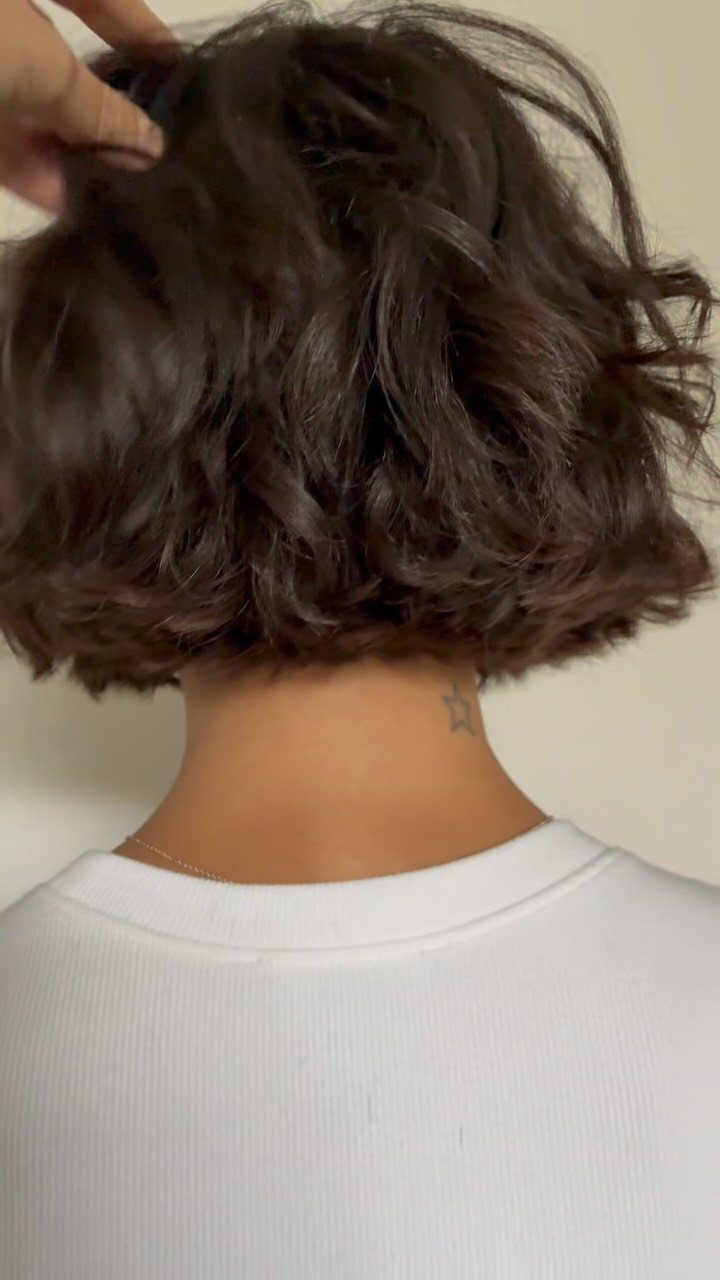 Short dark wavy bob lifted by a hand, showing textured layers at the back
