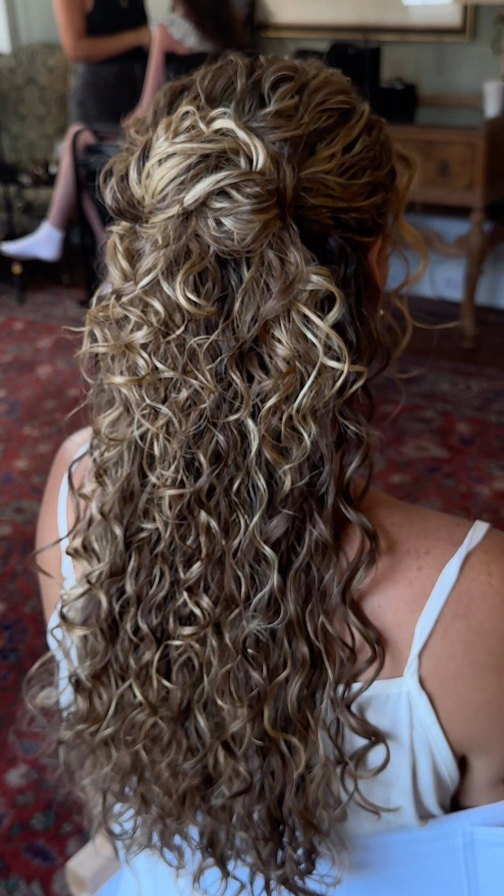 Pinned half-up curls cascade down the back of a person in a light blue dress