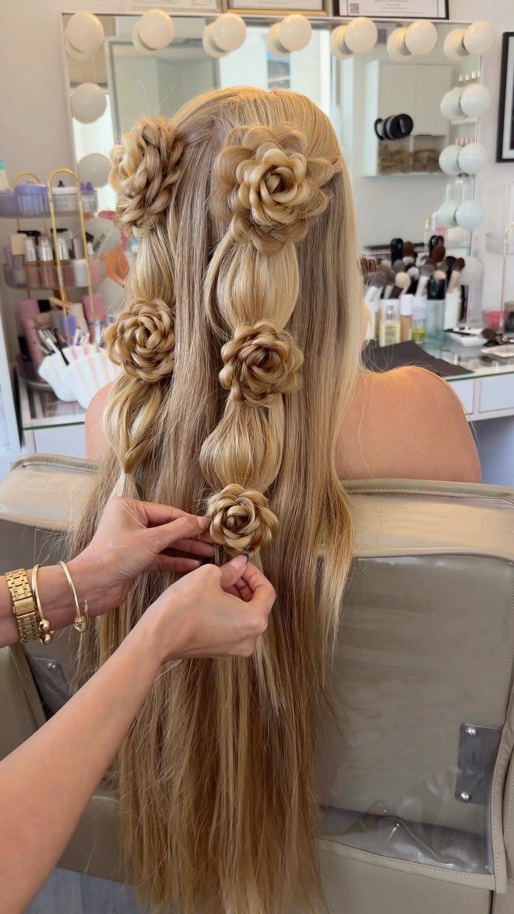 Blonde hair styled with several braided rose coils as hands pin one in place