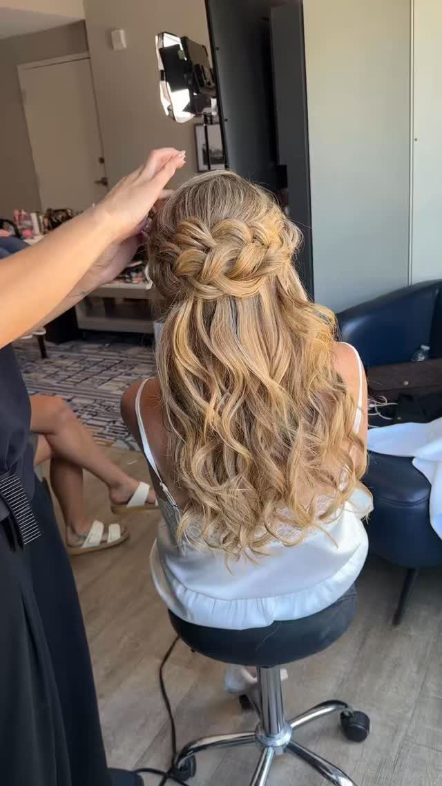 Thick blonde crown braid pinned above long loose curls in a salon