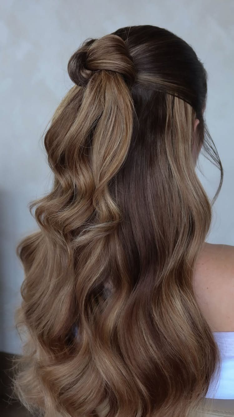 Long wavy brown hair gathered into a small half-up knot at the crown