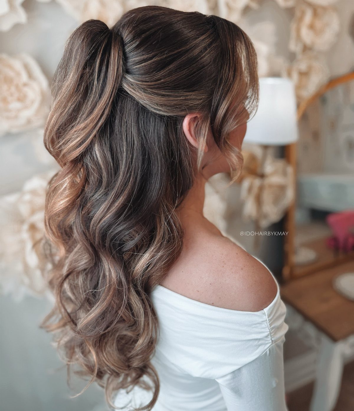 Pinned half-up brown hair with sculpted curls cascading over a white top