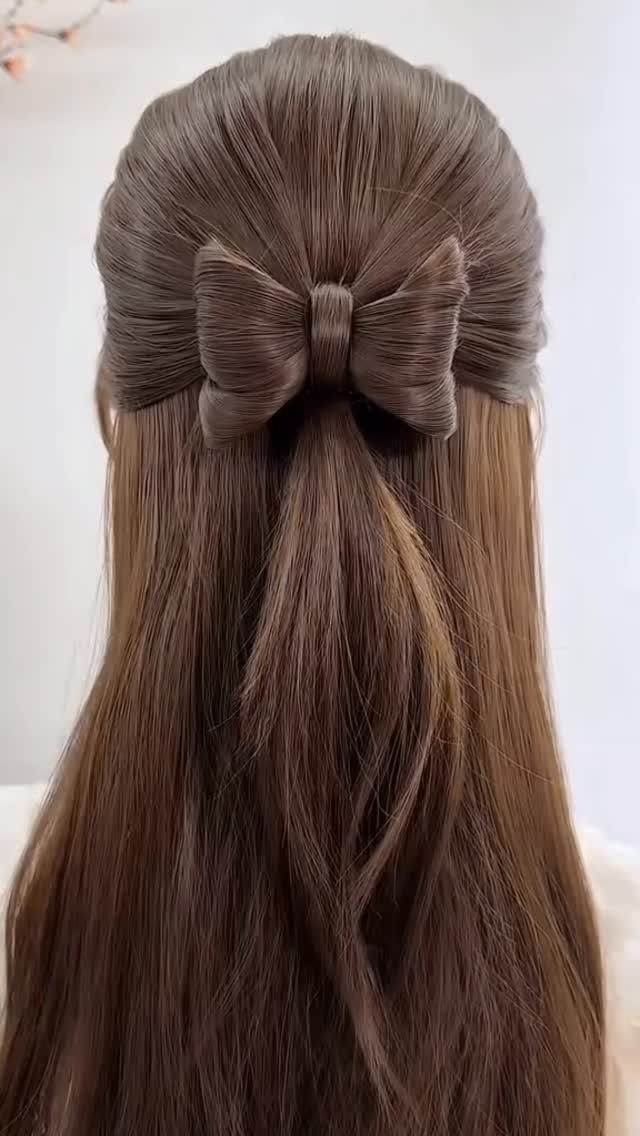 Long brown hair styled half up with a large, smooth bow made from hair