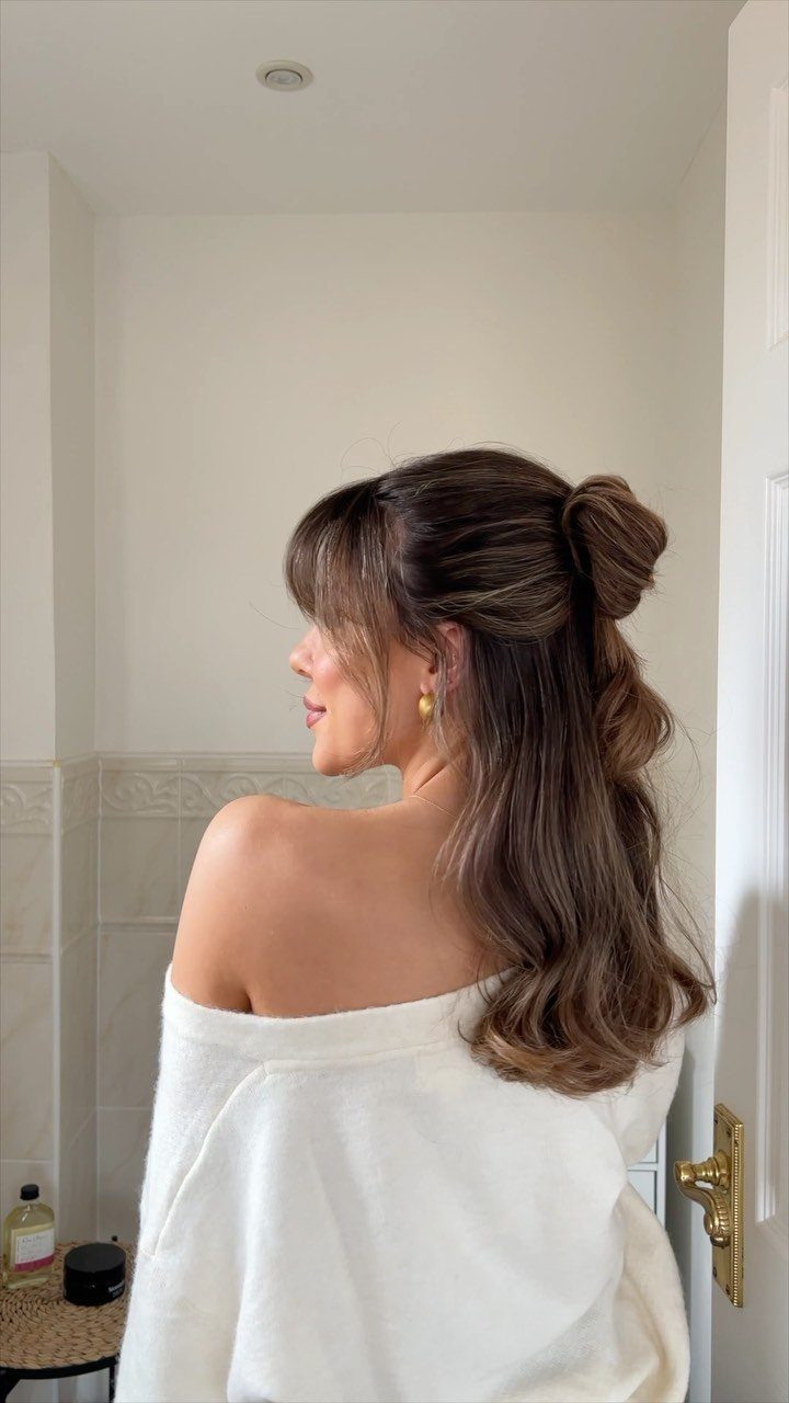 Woman with half-up brown hair, loose waves, and face-framing bangs in a bathroom