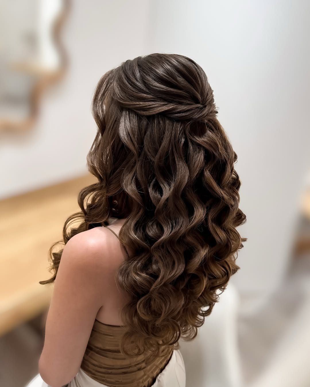 Long brunette mermaid curls fall beneath a voluminous swept half-up bouffant