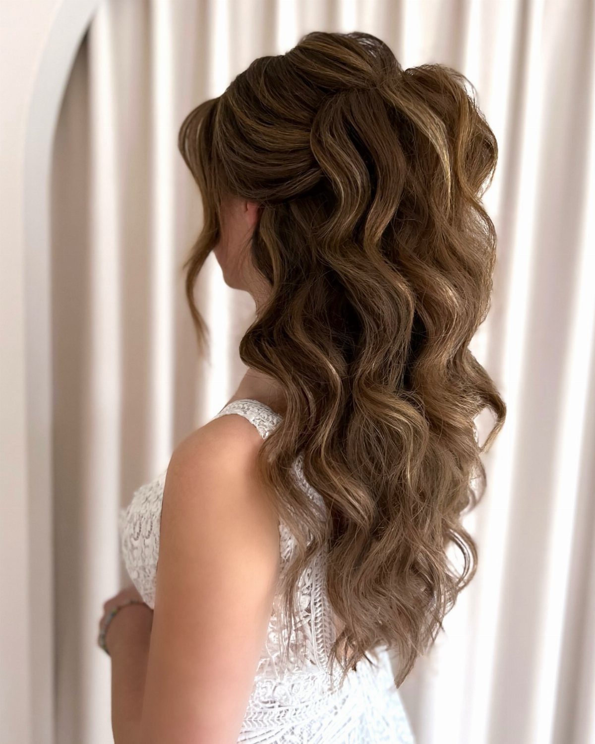 Woman with long curled brown hair styled in a voluminous twisted half-updo