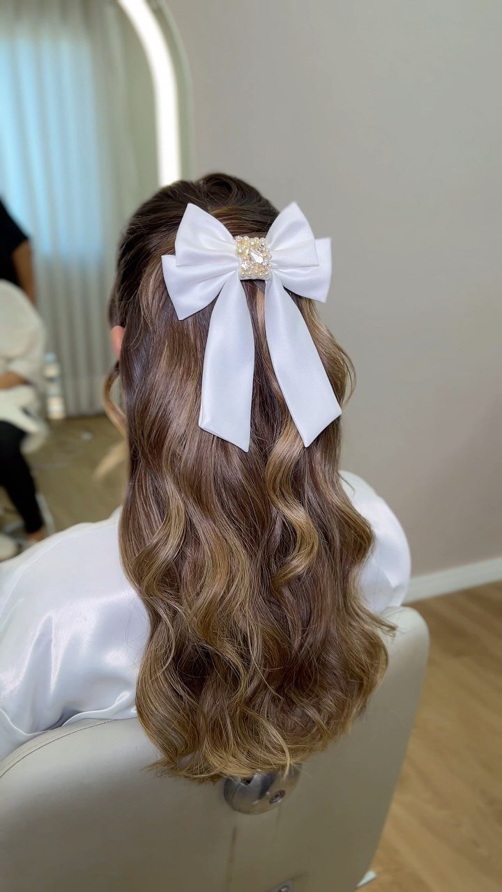 Half-up wavy brown hair tied with a large white ribbon bow
