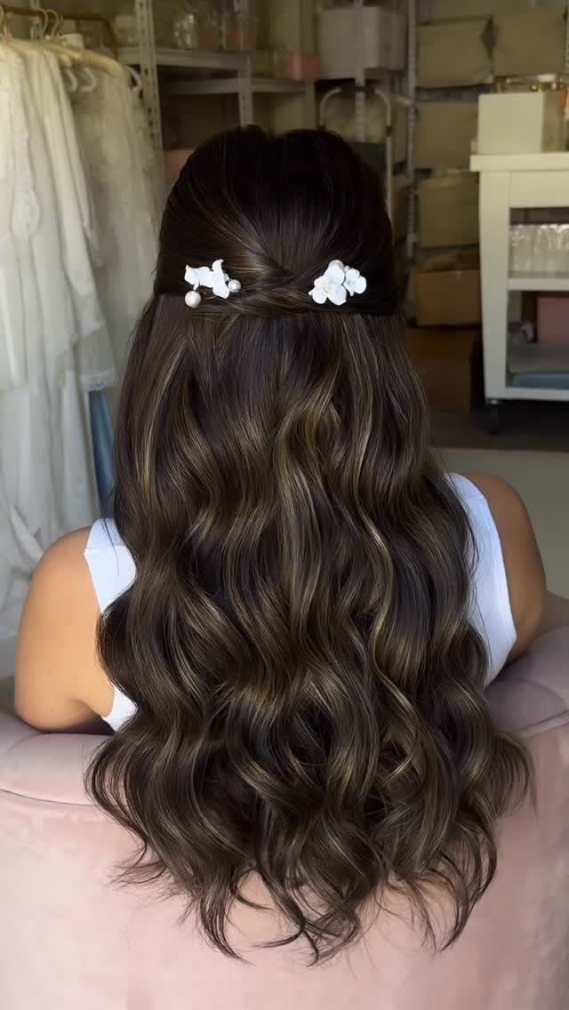Long dark curls styled in a twisted half-up look with white flower clips