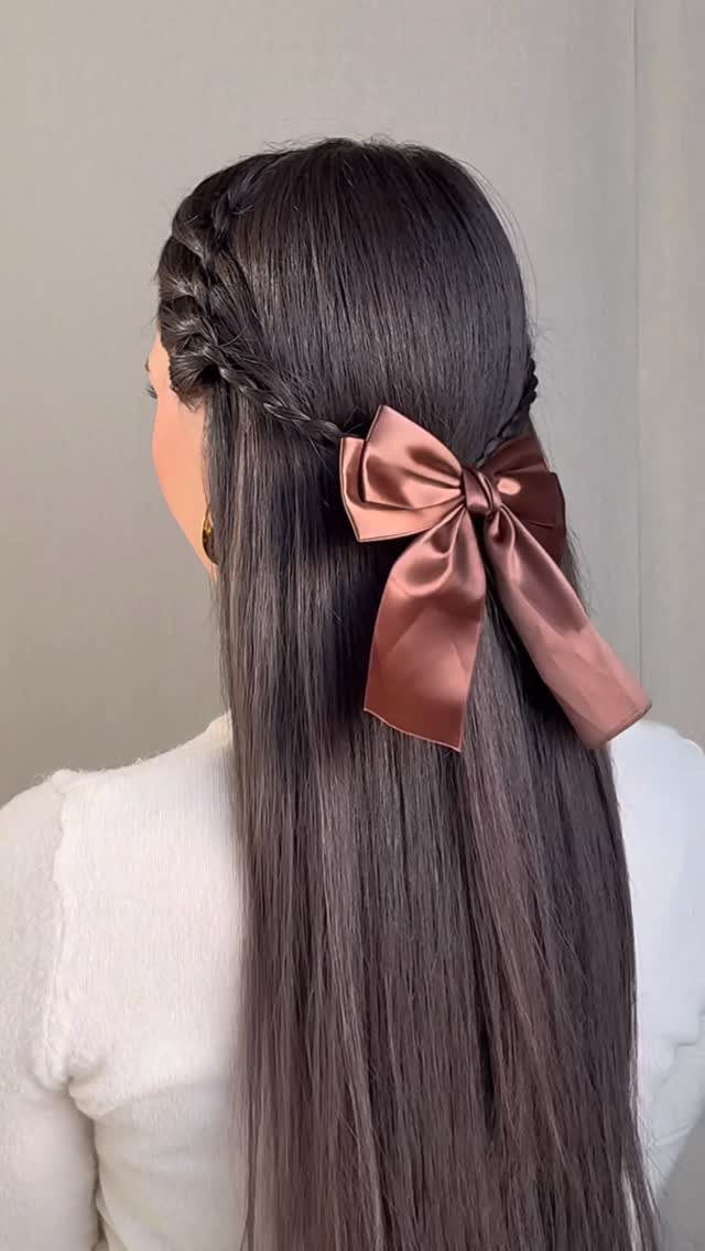 Long dark hair styled half up with a side braid and dusty-rose satin bow