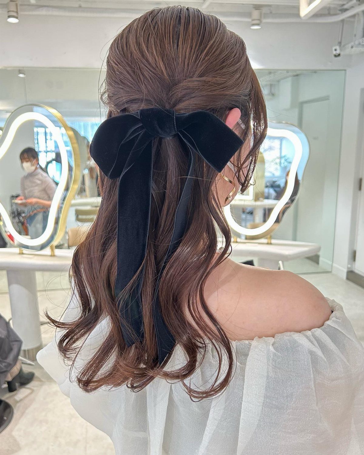 Half-up wavy brown hair secured with a large black velvet bow
