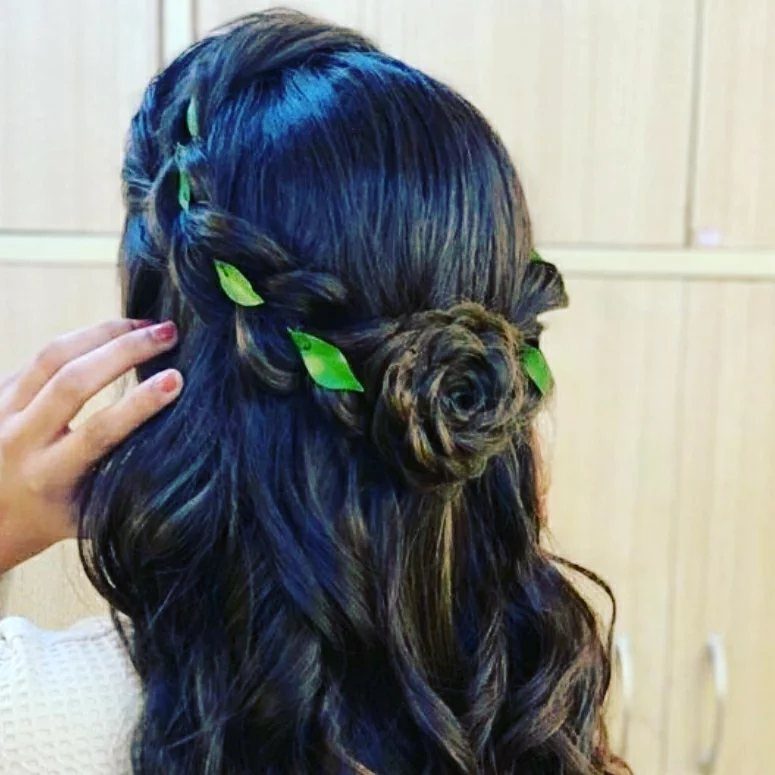 Dark wavy half-up hair with a braided rose and green leaves