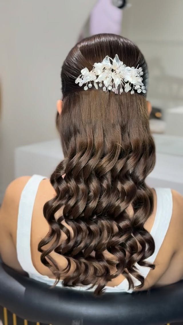 Long dark curls with a white floral hairpiece pinned into a half-up hairstyle
