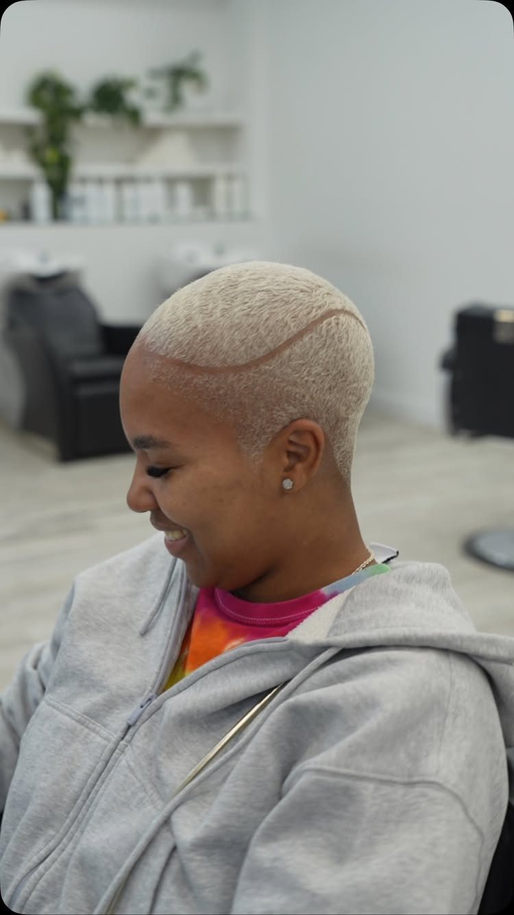 Person with short blond hair showing a curved shaved hard part line