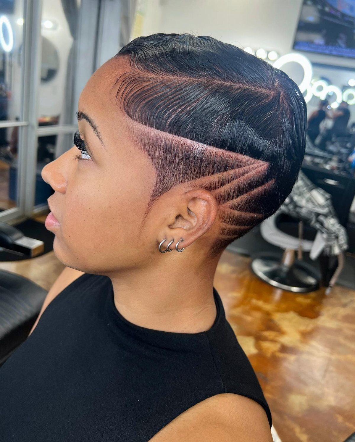 Short dark pixie with a high fade, shaved curved lines, and a defined side part