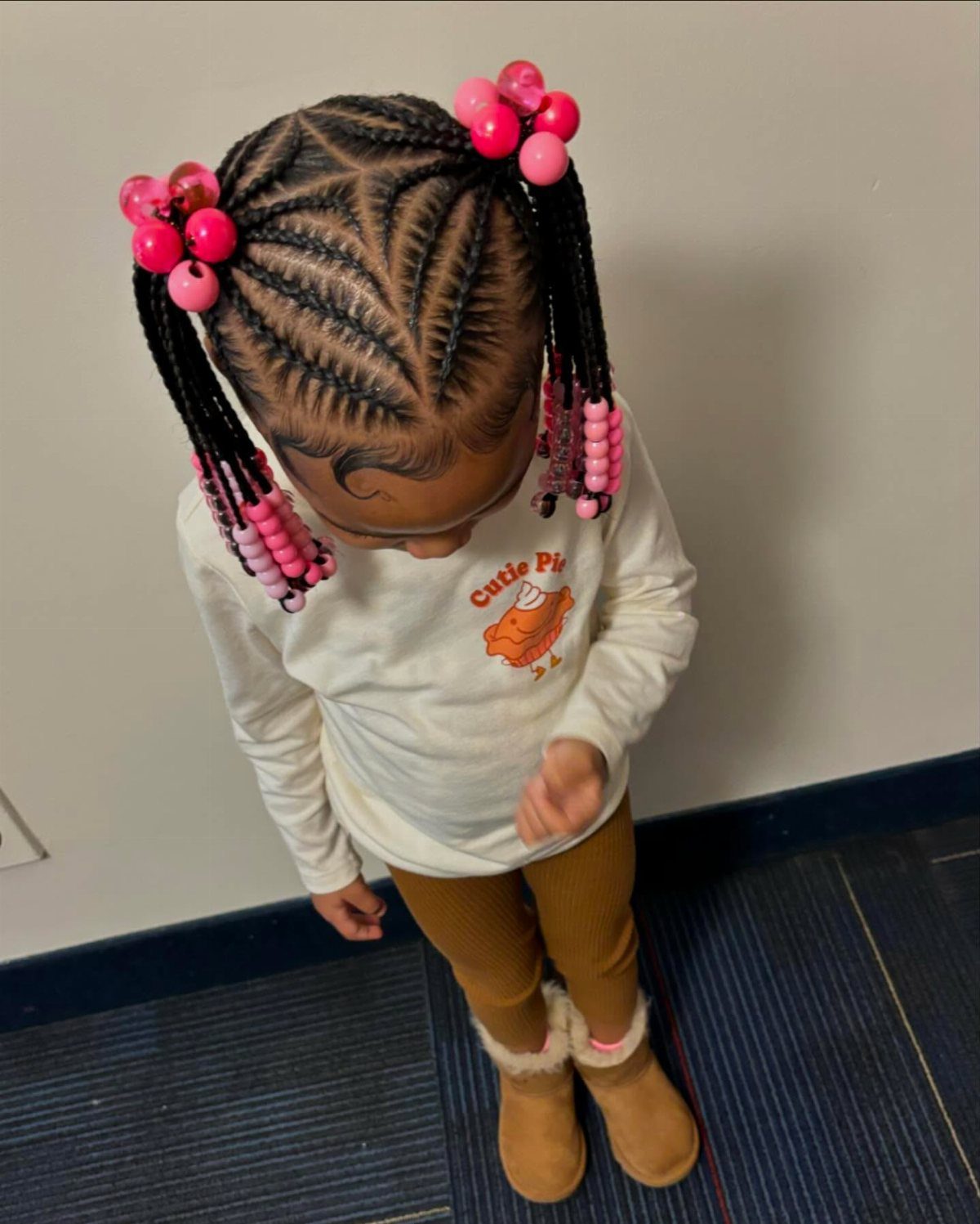 Child's geometric cornrows gathered into two high ponytails with pink beads and bows