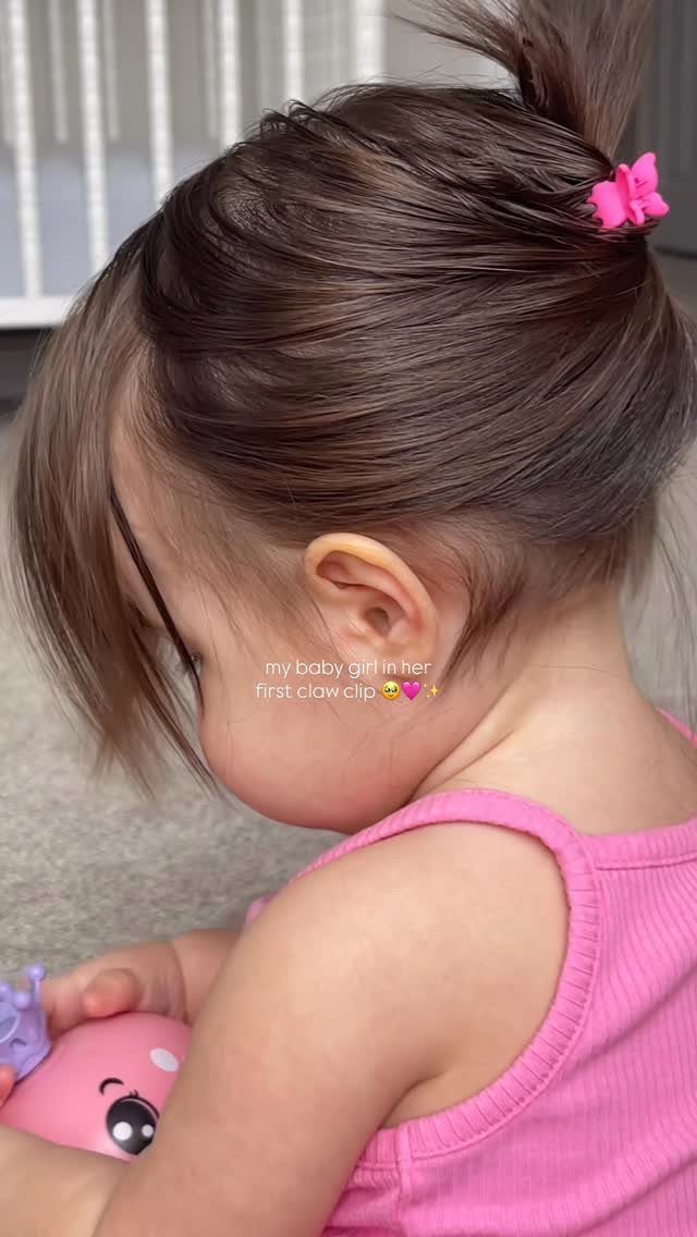 Child with dark brown hair pulled into a small ponytail with a pink flower clip