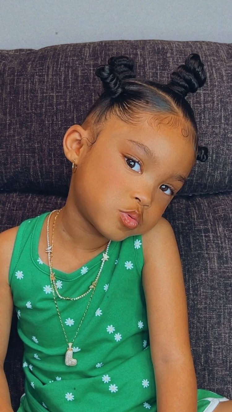 Child with two high coiled buns and smoothed edges, wearing a green top