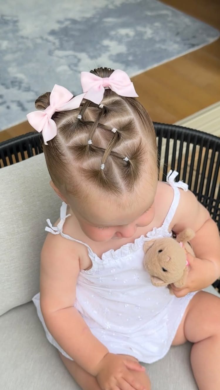 Baby with two sectioned ponytails, pale pink bows, white dress, and plush toy