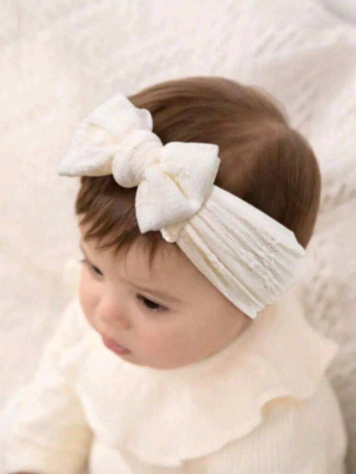 Baby with short brown hair wearing a wide white bow headband