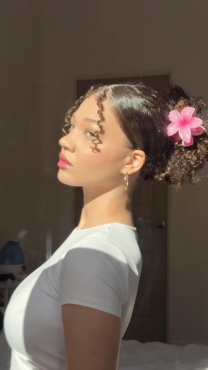 Woman with tightly curled fringe parted at the center and a flower in her bun