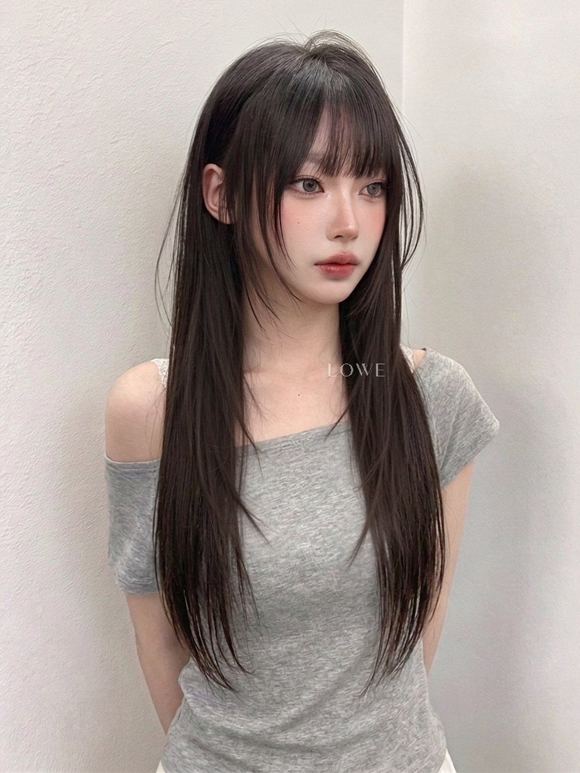 Woman with long, straight dark hair and blunt bangs wearing a gray top