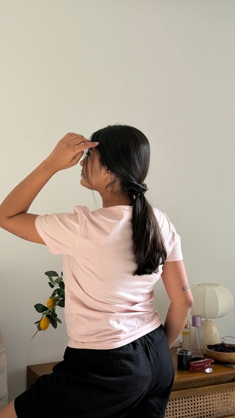 Woman gathers long dark hair into a low ponytail