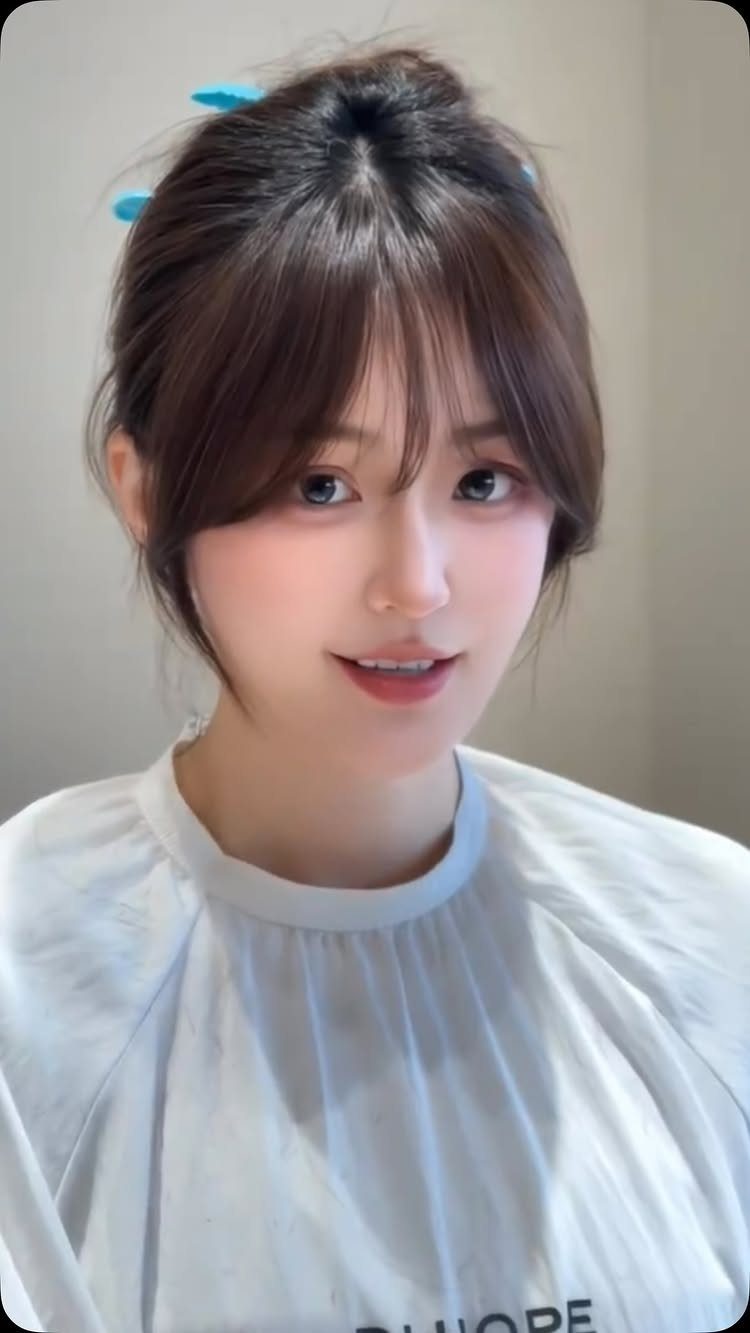 Young woman with dark hair and airy see-through bangs wearing a white salon cape