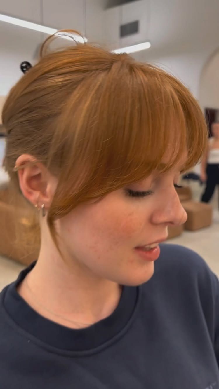 Auburn-haired person showing long, side-swept bangs in a salon